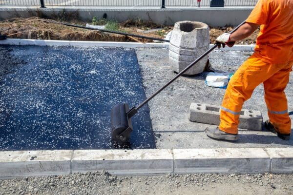 Worker push asphalt wooden hand roller on hot asphalt pavement with gravel.