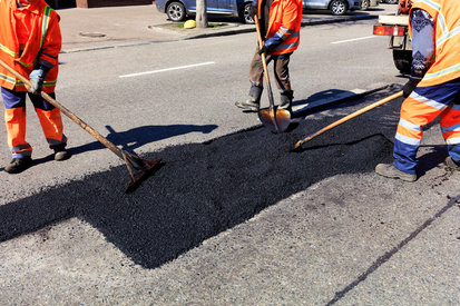The working team of asphalt builders piles up fresh asphalt on a part of the driveway and levels it for repair.