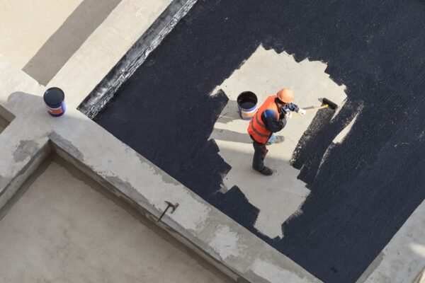 The worker in overalls applies an insulation coating on the concrete surface