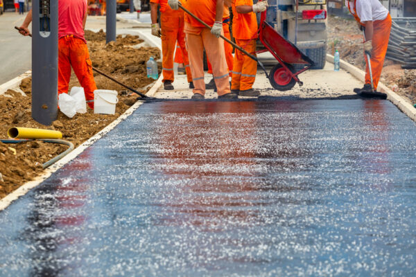 Workers melting and placing asphalt pavement with gravel.