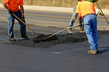 Workers smoothing out asphalt pavement at the end of the run for a new road